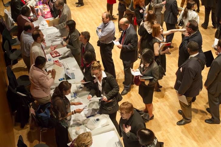 Dozens of job seekers attend a job fair in their black suits contrasted against light wood floors